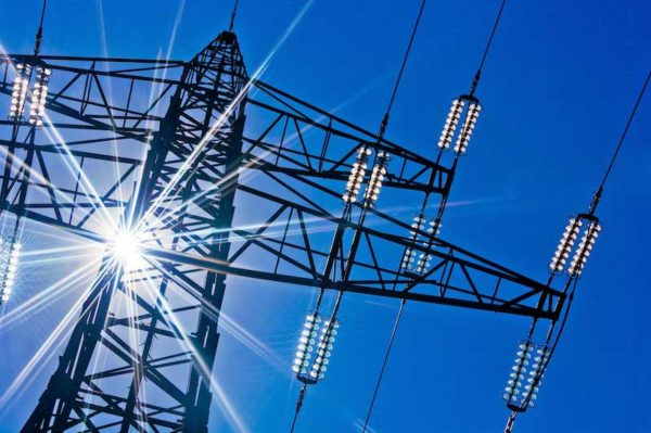 an electricity tranmission tower and wires against a blue sky with a solar flare. It is from viewpoint of looking up from the ground.