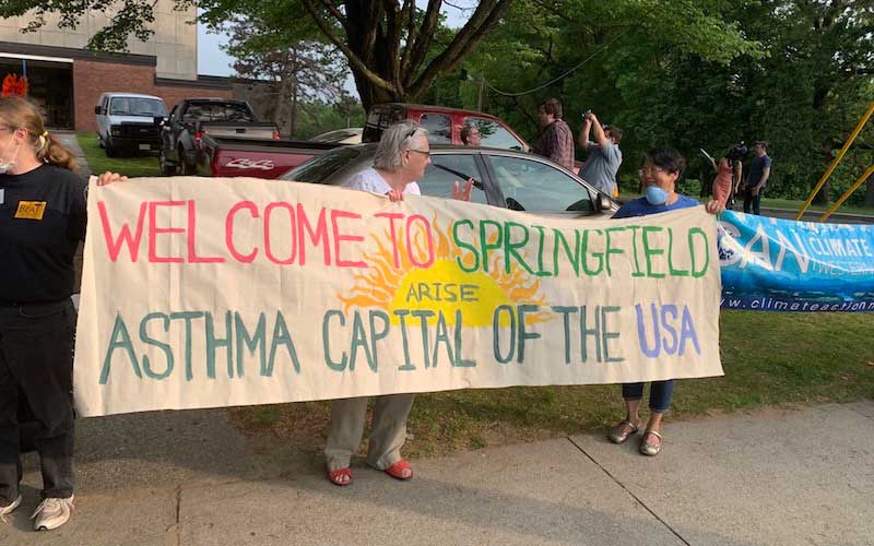 Community members holding a banner reading "Welcome to Springfield the Asthma Capital of the USA" to oppose a proposed biomass plant.