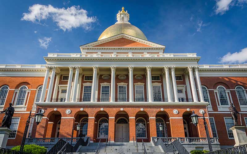 The front of the Massachusetts State House, with the gold dome visible in front of blue sky