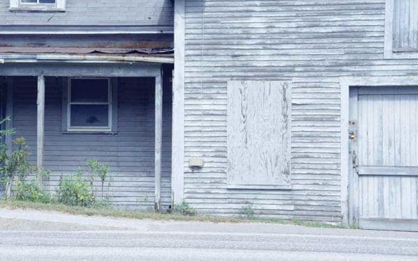 The side of an old house with white wooden slats. The paint is peeling.