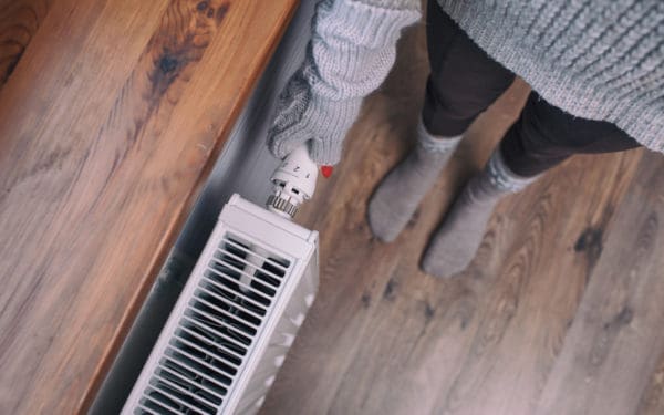 Image: a person wearing mittens turns on a radiator.