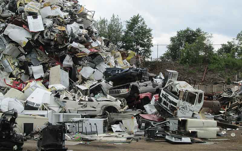 A scrap metal facility with a large pile of rusted cars, trucks and other trash.