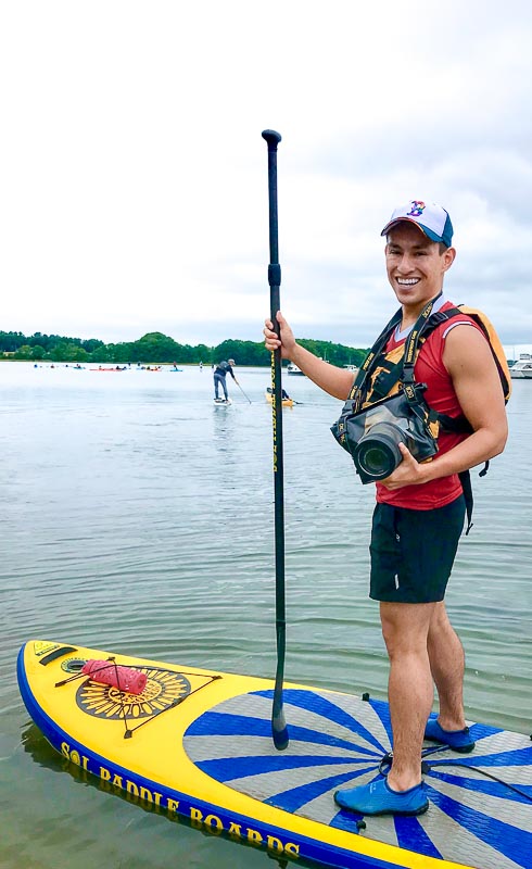 Adilson Gonzalez, CLF Communications Strategist, holding a camera on a stand-up paddleboard.