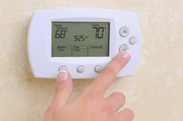 A hand adjusts the temperature on a thermostat to 70 degrees Fahrenheit.