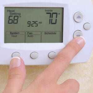 A hand adjusts the temperature on the thermostat to 70 degrees Fahrenheit.