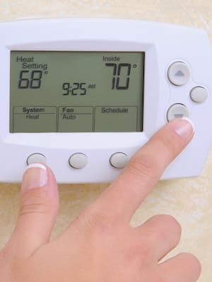 A hand adjusts the temperature on the thermostat to 70 degrees Fahrenheit.