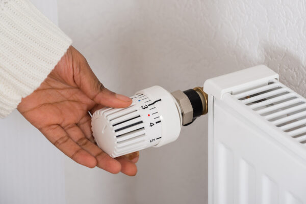 A hand turns the dial on a thermostat attached to a radiator to adjust the temperature.