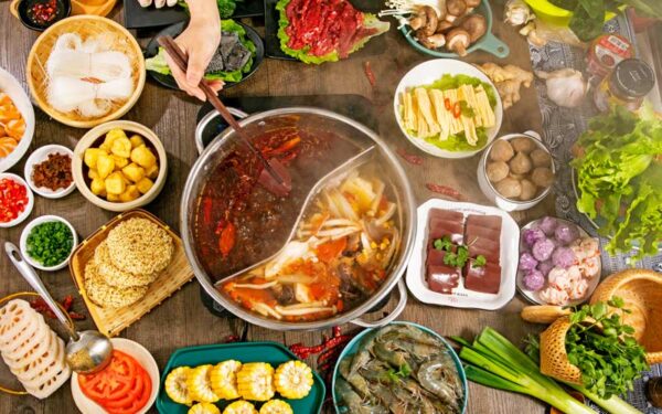 Table with hot pot surrounded by vegetables, meats, and toppings for Chinese cookout. Image illustrates well-planned menu to avoid food waste and leftovers.