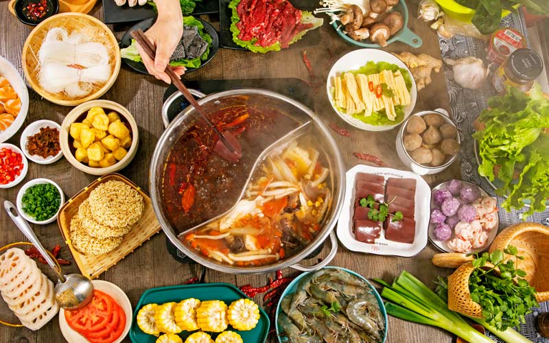 Table with hot pot surrounded by vegetables, meats, and toppings for Chinese cookout. Image illustrates well-planned menu to avoid food waste and leftovers.
