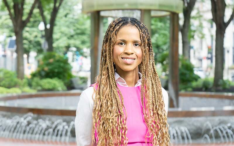 Portrait photography of Britteny Jenkins, Environmental Justice Vice President at Conservation Law Foundation. The background shows lush greenery and a green-tarnished metal fountain at Post Office Square in central Boston.