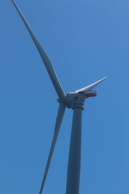 Photo showing three blades of an offshore wind turbine against a deep blue sky.