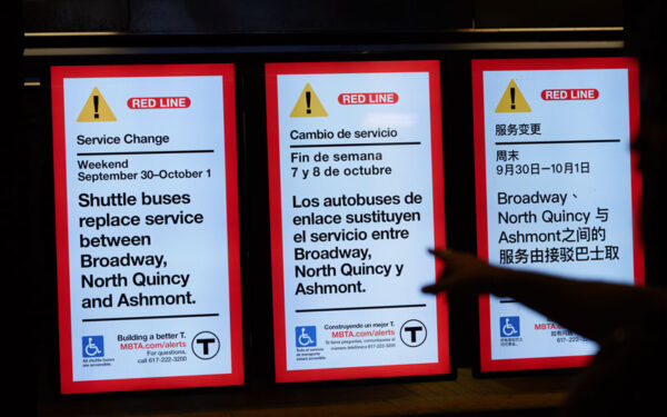 3 digital displays announcing MBTA closures of the Red Line in three different languages: English, Spanish, and Chinese. Shadow of hand pointing to the signs.