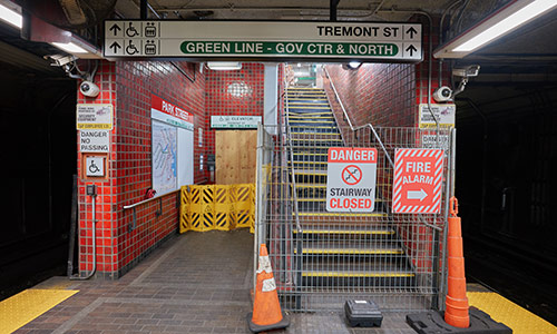 Photo of stairs and elevators in Park Street station of the Red Line. Both areas are closed and have multiple signs of danger, warnings, and alarms. Orange cones on the front. 