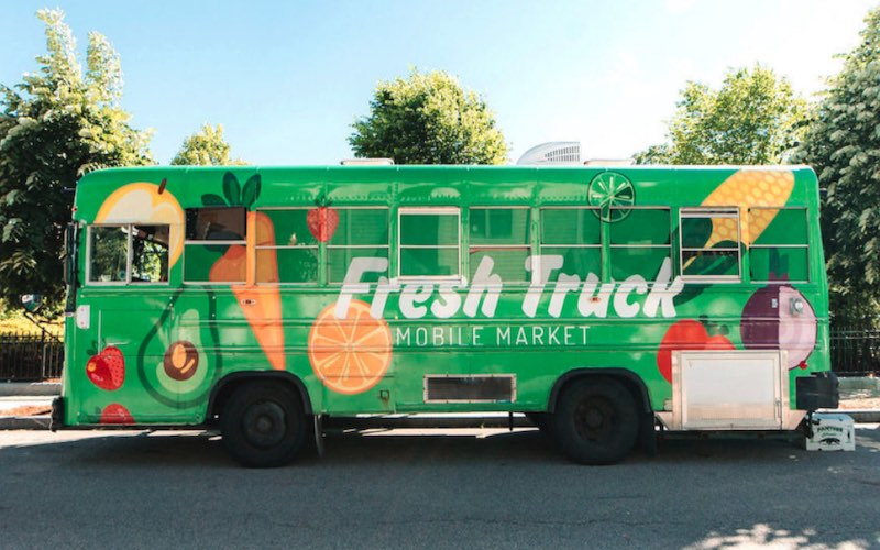 A green bus with the words Fresh Truck and images of healthy food on the side is shown