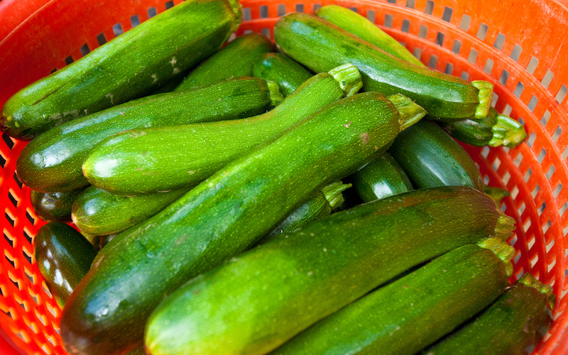 An overhead close up of a pile of zucchini in an orange basket.