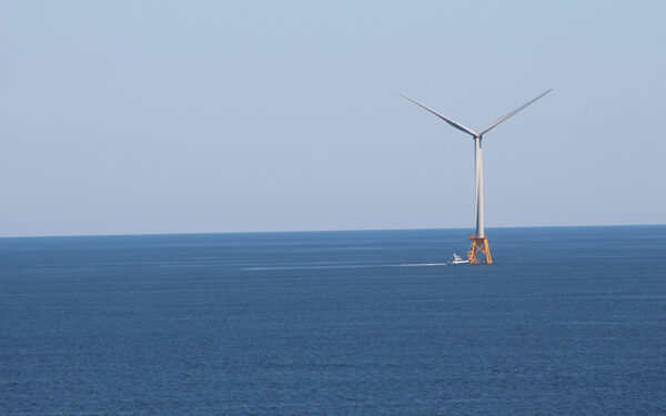 Offshore wind turbine on a calm ocean, being approached by a boat.