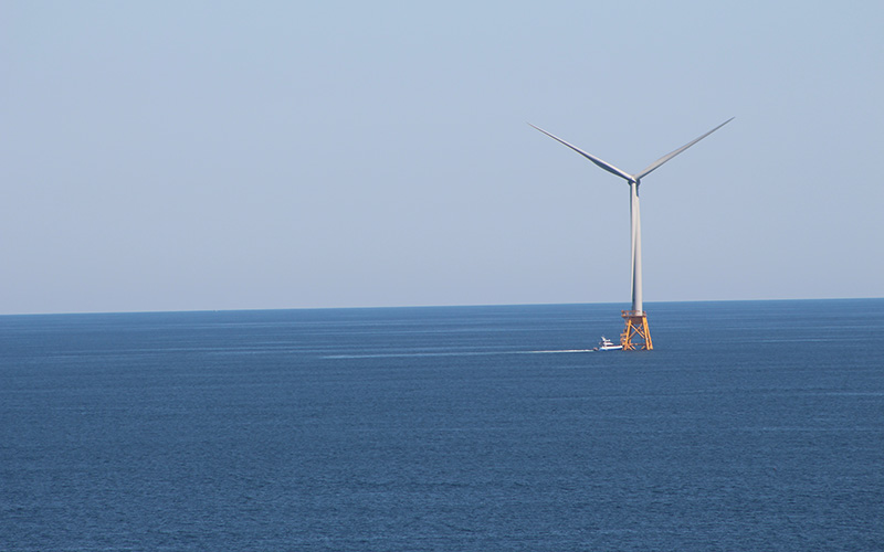 Offshore wind turbine on a calm ocean, being approached by a boat.