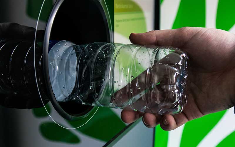 A person places a plastic water bottle into a bottle redemption machine.