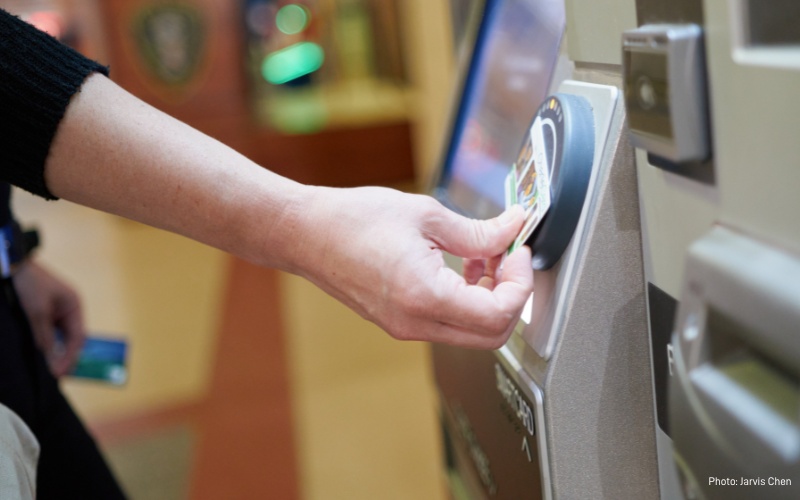 Photo of MBTA fare machine and customer tapping card on sensor to purchase additional fare. Under new reduced fare program, eligible customers will qualify for a discount of half or more.