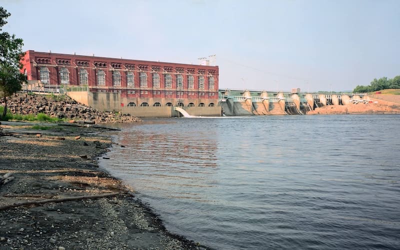 A brick building and hydroelectric dam with the water of the Connecticut River in the foreground