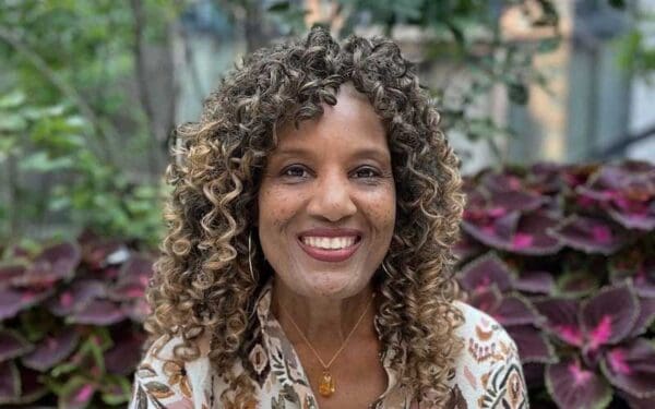 A black woman with shoulder-length curly hair smiles into the camera