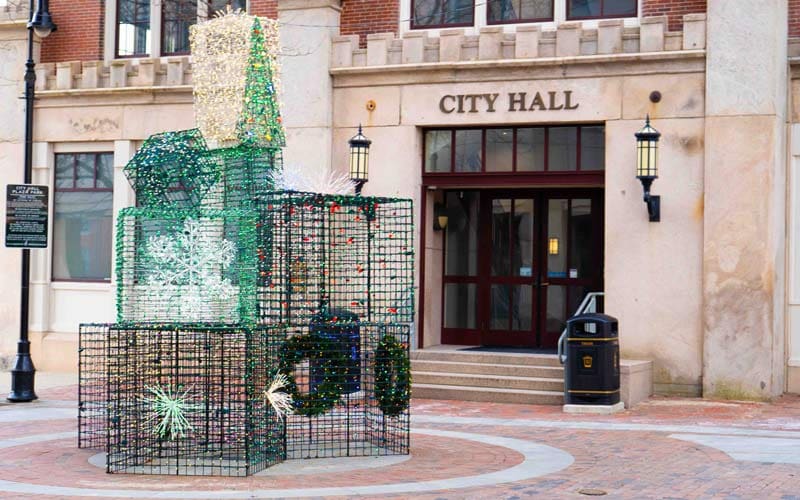 Front entrance of Manchester City Hall decorated with a holiday sculpture made of wire and lights, including snowflakes and wreaths.