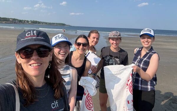 CLF staff members on a beach holding bags of garbage and a clipboard