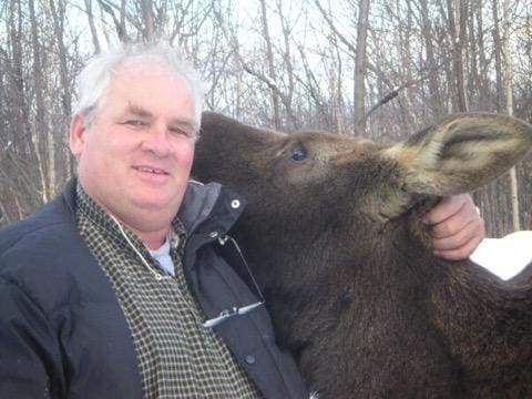 Eric Orff with his arm around a moose whose face is snuggled into his shoulder.